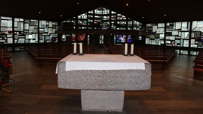 Ein moderner Altar in einer großen, dunklen Kirche mit vielen Fenstern.