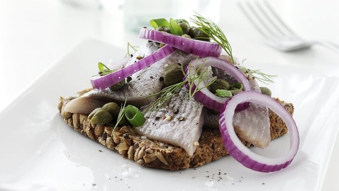 Grillet fisk toppet med løg, urter og kapers serveret på fuldkornsristet brød.