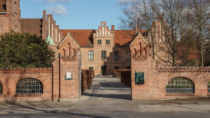 Det er et stort, gotisk teglsteinshus med spisse tårne og en indgangsport med mur og jernskærme.