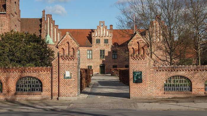 Det er et stort, gotisk teglsteinshus med spisse tårne og en indgangsport med mur og jernskærme.