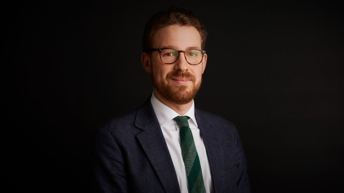 Professionel mand i jakkesæt, briller og slips, der poser mod en mørk baggrund.