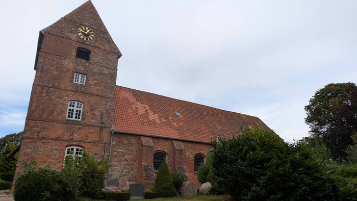 Alte Backsteinkirche mit hohem Turm und Zifferblatt.