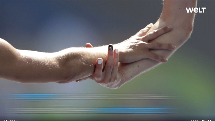 Zwei Hände halten sich fest, eine trägt eine Armbanduhr, im Hintergrund ein unscharfes Landschaftsbild.