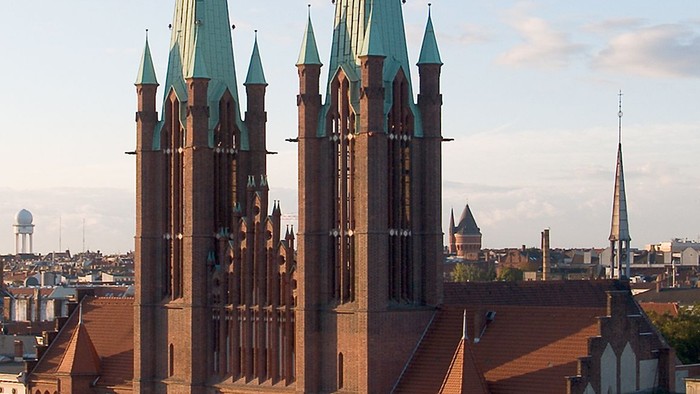 Große Kirche mit zwei hohen Türmen inmitten von Gebäuden und Bäumen.