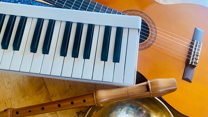Ein Gitarre, ein Keyboard und ein Xylophon liegen auf einem Holzboden