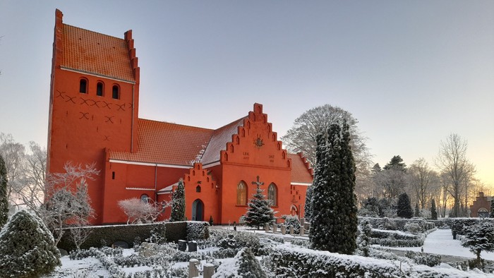 Rødt kirke med snødekt have og træer