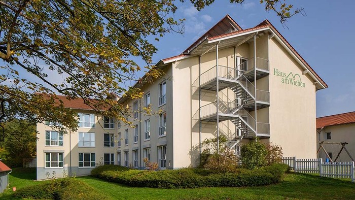 Ein modernes Wohngebäude mit Balkonen und Treppenhaus, umgeben von Grünflächen und Bäumen.