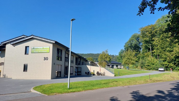 Ein modernes Gebäude mit der Nummer 30 und einem grünen Schild, umgeben von Bäumen und einem klaren blauen Himmel.