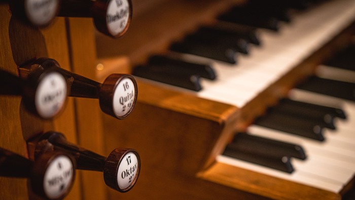 Nærbillede af et orgels træstoppers knopper og klaverlignende tangenter i varmt lys.