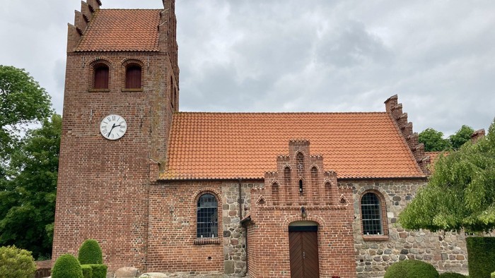 Historisk murstenskirke med klokketårn, omgivet af velplejet grønt og stenmure.