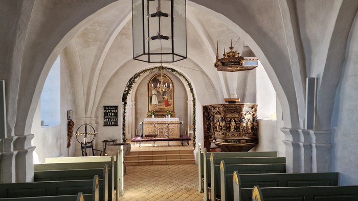 Indre del af kirke med bænke, lysstake og alter.