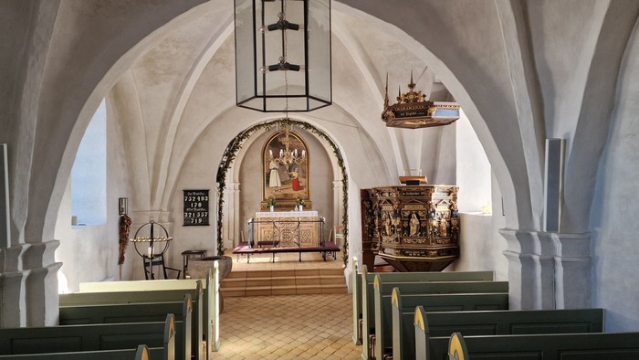 Indre del af kirke med bænke, lysstake og alter.