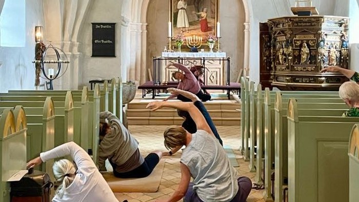 Mennesker laver yoga-strækøvelser inde i en historisk kirke med grønne kirkebænke og prægtige dekorationer.