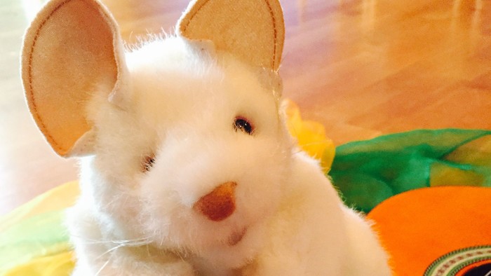 Et hvidt musekudde sidder med tre fargefulde æg og en guitar.