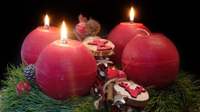 Fire røde stearinlys på en mørk baggrund, omgivet af grantrægrene og kogler.