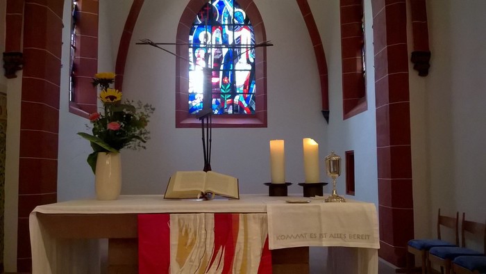 Ein Altar in einer Kirche mit Kerzen, Blumen und einem farbenfrohen Fenster.