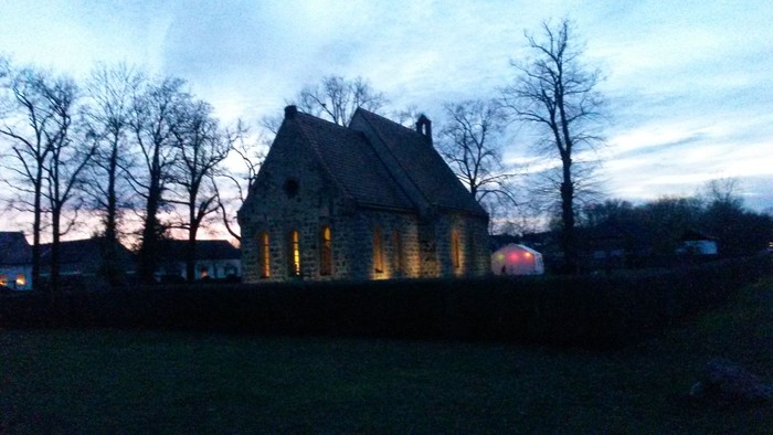 Ein altes Haus mit spitzem Dach und Bäumen im Vordergrund bei Dämmerung