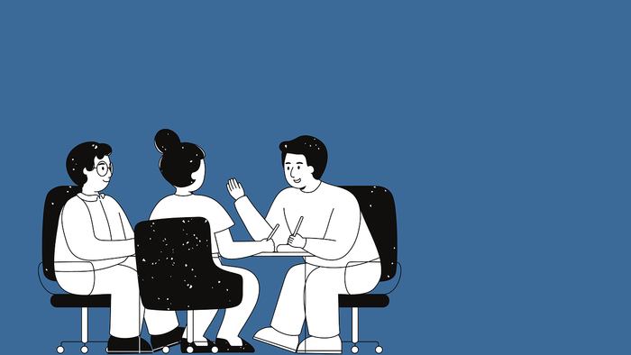 Tre personer i et møde, hvor én gestikulerer, mens vedkommende holder en clipboard og nogle papirer.