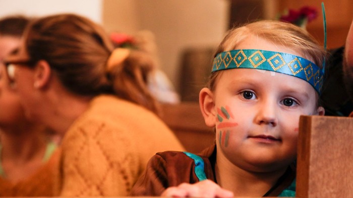 En ung dreng med ansigtsmaling og pandebånd kigger på kameraet.