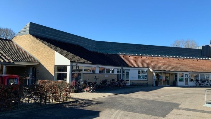 Et moderne bygning med fladt tag og store vinduer, med cykler og bus i nærheden