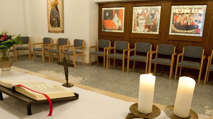 Eine friedvolle Kapelle mit Kirchenbänken, religiösen Kunstwerken, einem offenen Buch auf einem Lesepult und brennenden Kerzen.