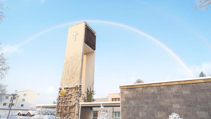 Verschneite Kirche Neu-Buckow bei Sonnenschein und Regenbogen im Hintergrund