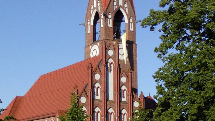 Kirchturm mit spitzem Dach und Uhr, umgeben von Bäumen