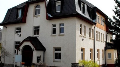 Das Bild zeigt ein zweistöckiges Gebäude mit einem Kreuz auf dem Dach.