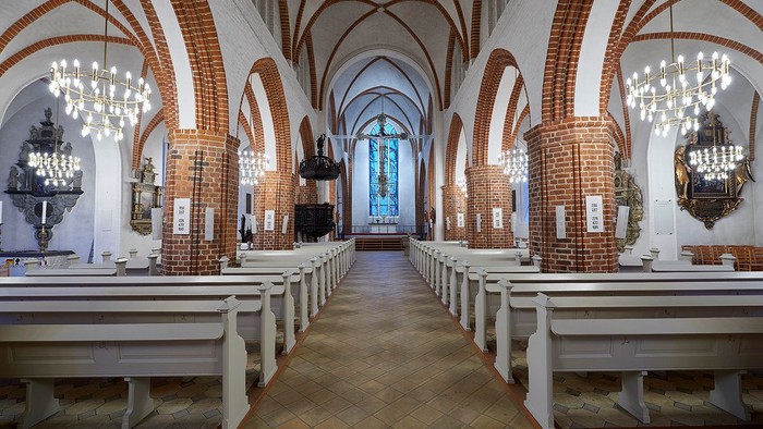 Indre del af kirke med hvide bænke og høje buer.