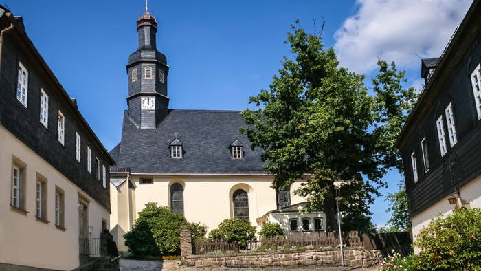 Kirchengrundstück mit schwarzem Turm und weißem Gebäude, umgeben von Bäumen und Häusern