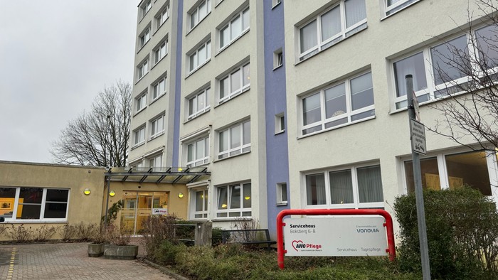 Modernes Wohngebäude mit farbigen Fassaden und Eingangsbereich, daneben ein rotes Schild mit weißer Beschriftung.