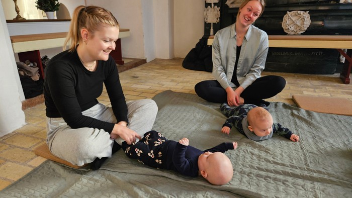 To voksne og en baby, der sidder på et tæppe i en stue.