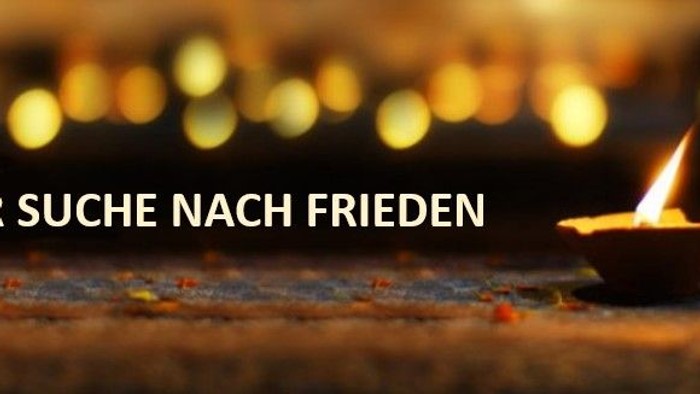 Eine brennende Kerze vor einem unscharfen Hintergrund mit Lichtern und dem Text „Auf der Suche nach Frieden“.