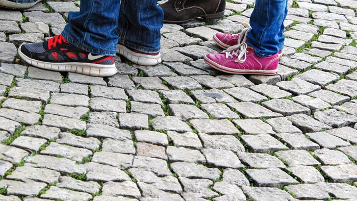 Drei Personen stehen auf Kopfsteinpflaster, ihre Schuhe sind bunt und unterschiedlich.