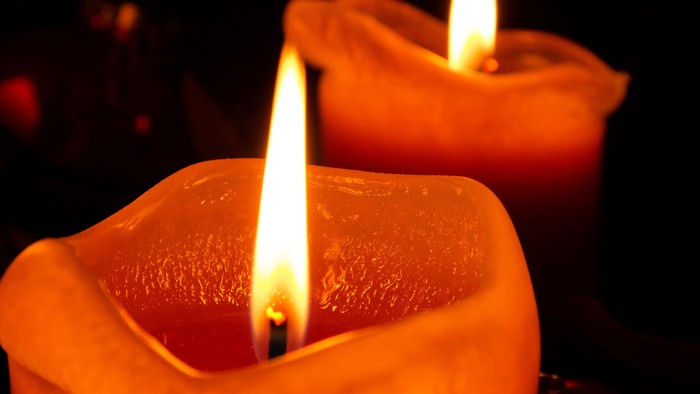 Zwei brennende Kerzen in orangefarbenen Haltern.