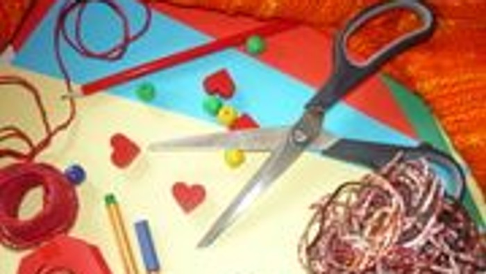 Das Bild zeigt Bastelutensilien wie Schere, Perlen und Stoffreste auf einem Holztisch.