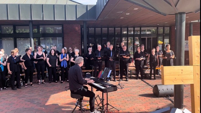 Eine Gruppe von Menschen singt und spielt Musik vor einem Gebäude.
