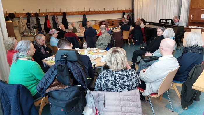 Eine Gruppe älterer Menschen sitzt in einem Raum und ist in Gespräche vertieft.