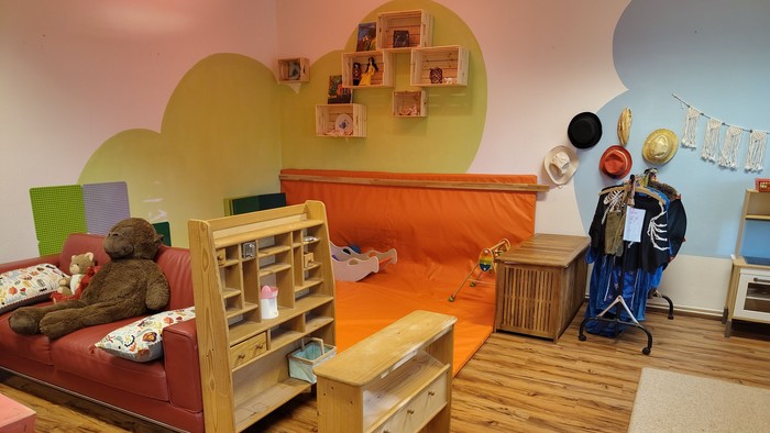 Ein für Kleinkinder gestalteter Raum mit Kaufmannsladen, Spielmatte und Sofa