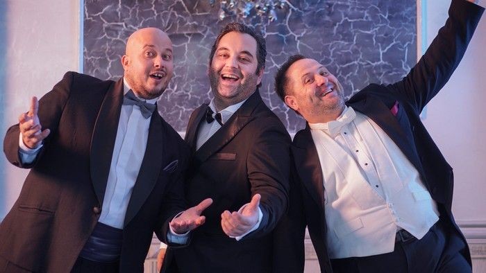 Drei Männer in Anzügen posieren spielerisch zusammen.