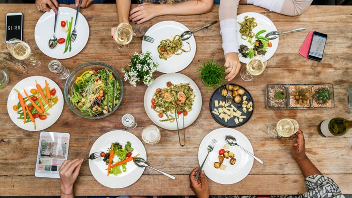 Eine Gruppe von Menschen genießt ein gemeinsames Essen mit verschiedenen Gerichten und Getränken an einem Holztisch.