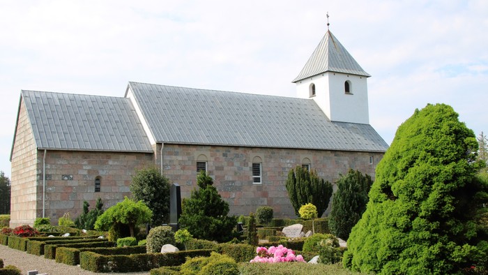 En smuk kirke med et tårn og en hage med grønne planter og blomster.