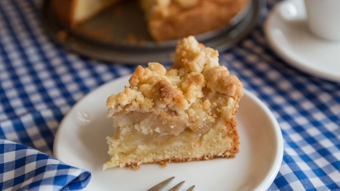 Ein Stück Apfelkuchen auf einem Teller mit Gabel, daneben eine Kaffeetasse