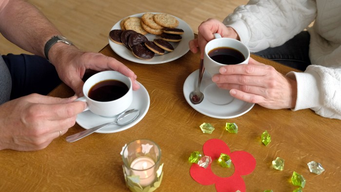 Zwei Personen trinken Kaffee und essen Kekse an einem Tisch.