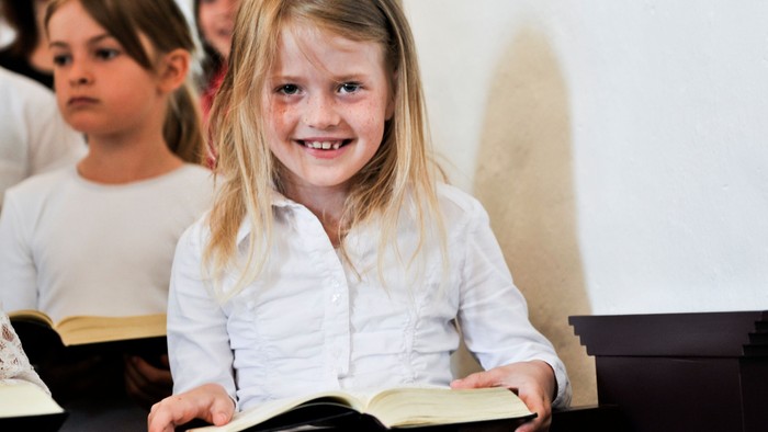 En lille pige med blond hår læser i en bog i en klassesal.