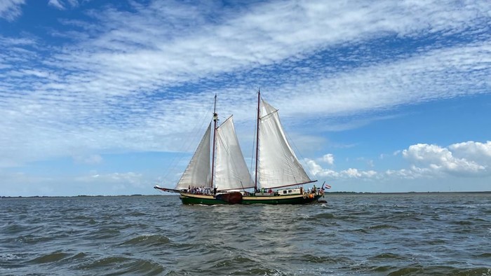 Segelboot mit zwei Masten, das auf ruhiger See unter blauem Himmel mit weißen Wolken segelt.