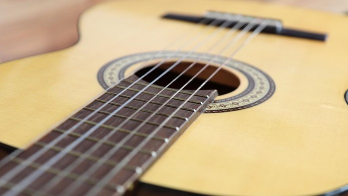 Nahaufnahme einer akustischen Gitarre mit hellem Korpus und dunklem Griffbrett und Saiten.