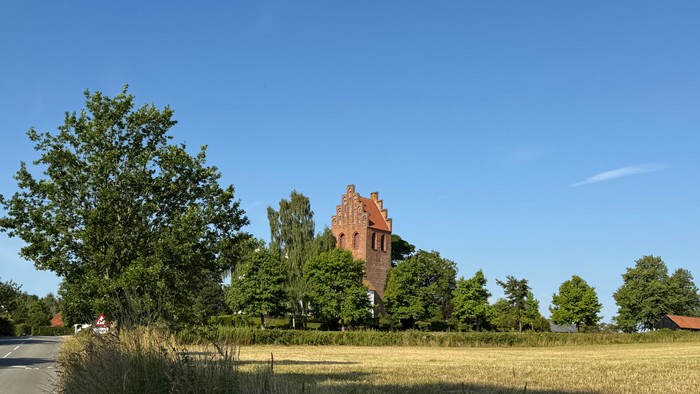 En rustik murstens tårn står midt i frodig grønne omgivelser under en klar blå himmel.