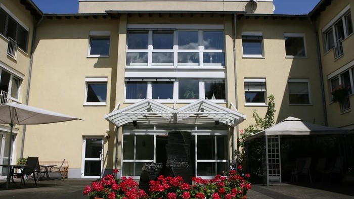 Ein charmanter Gebäudeeingang, geschmückt mit lebhaften Blumen, großen Fenstern und Sitzplätzen im Freien unter Sonnenschirmen.