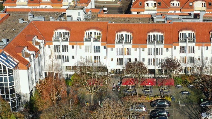 Moderner mehrstöckiger Gebäudekomplex mit roten Ziegeldächern, umgeben von einem Parkplatz und Bäumen.